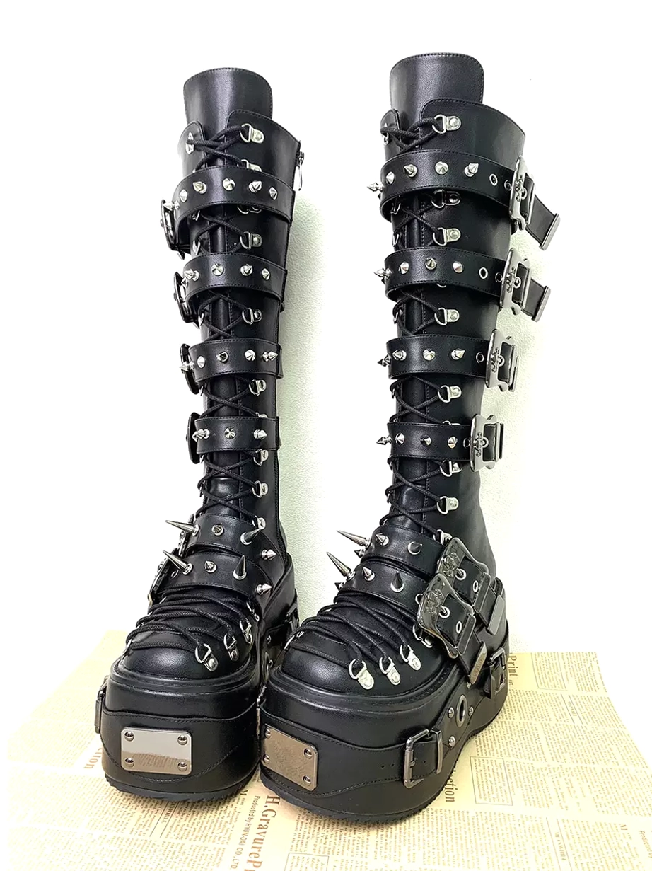 Front three-quarter view of black Gothic Lolita boots with metal toe plates, rivet decorations, and buckled straps displayed on vintage newspaper background