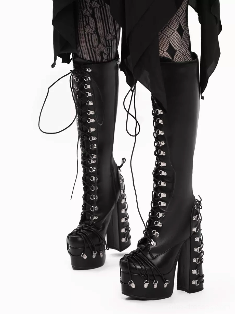 Black platform lace-up boots side-front three-quarter angle showcasing tall boot shaft, silver heel hardware, and trailing decorative laces with model in fishnet tights