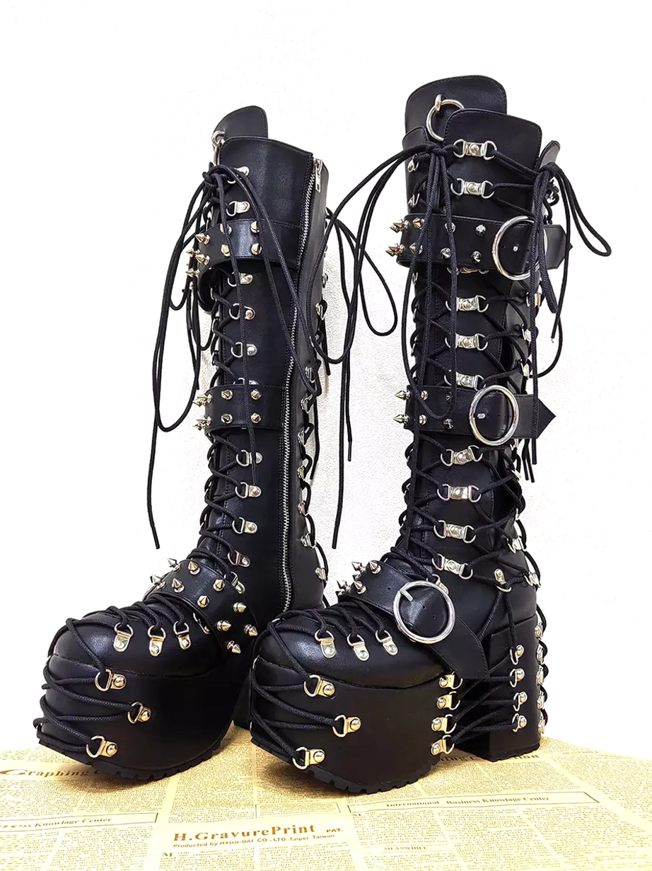 gothic lolita knee-high boots pair vintage newspaper background black leather silver grommets buckles lace-up decorations front view