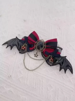 gothic lolita red-black striped bow hair clip with glossy black bat wings metal chains and vintage gem ornament flat lay on white knitted fabric with pearl decorations front view