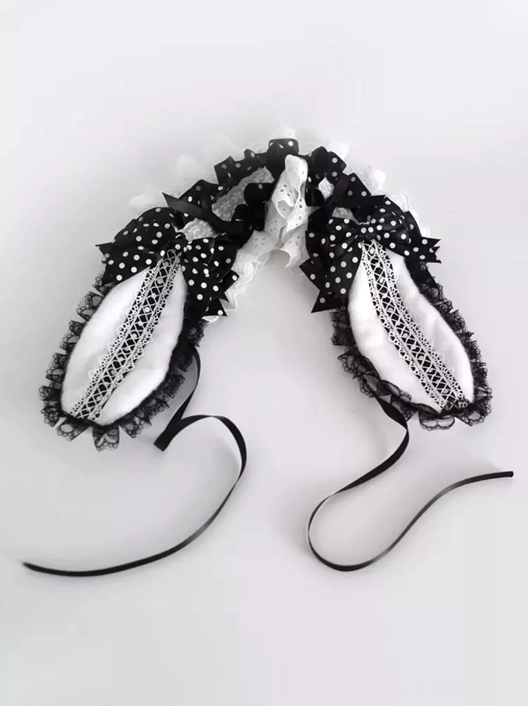 Flat lay top-down view of black Lolita bunny ear hairband showing polka dot fabric, embroidered lace ear panels, and black ribbon ties