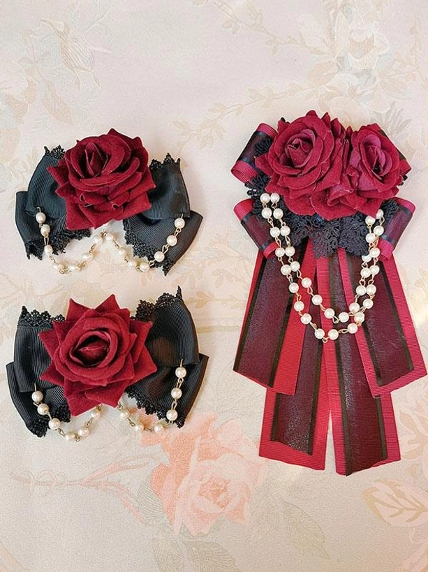 Gothic Lolita accessory set overhead flat lay view featuring black satin bows burgundy velvet roses faux pearl chains on vintage floral fabric background