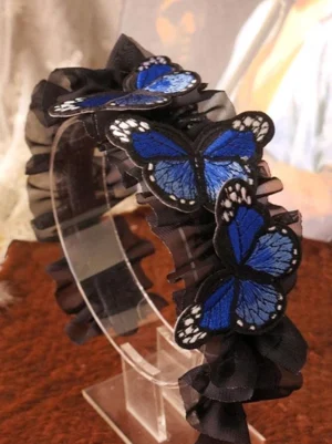 Gothic lolita ruffled butterfly hair headband with royal blue embroidered butterfly accents on black sheer ruffled band displayed on clear acrylic stand