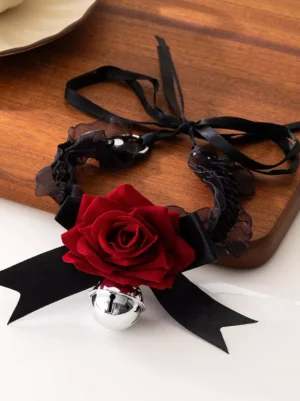 Gothic Lolita choker necklace with black lace satin band, red velvet rose, silver bell, and black ribbon bows displayed on wooden tray, top-down side view showing intricate design details and texture