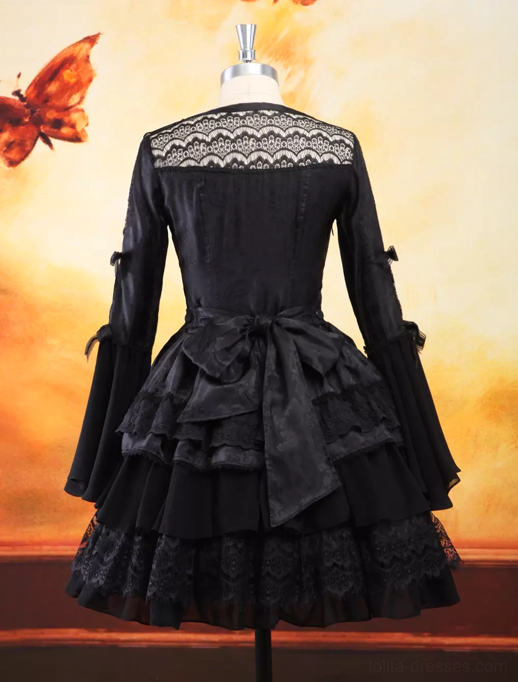 Rear full view of gothic lolita dress on dress form revealing lace back yoke, decorative waist bow, layered ruffled skirt construction, and sleeve details
