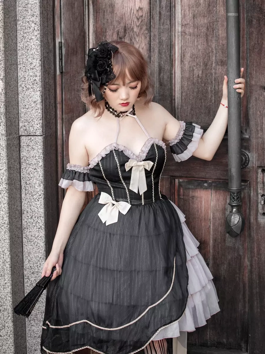 Gothic lolita dress black color front full-body view female model wooden door background off-shoulder ruffled cuffs halter neck bow decorations