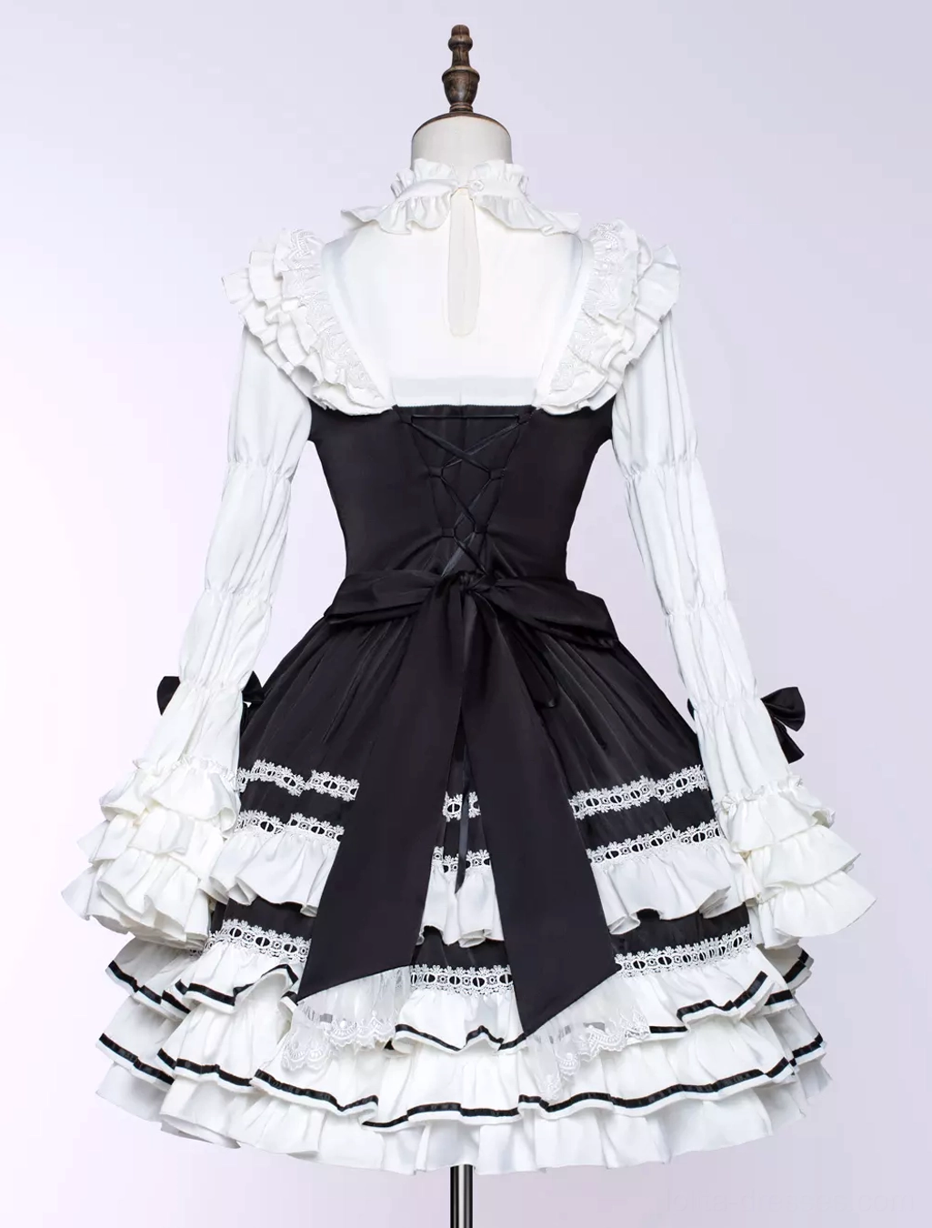 Black gothic lolita dress close-up showing bow necktie, crisscross lacing at chest, and decorative embellishment details