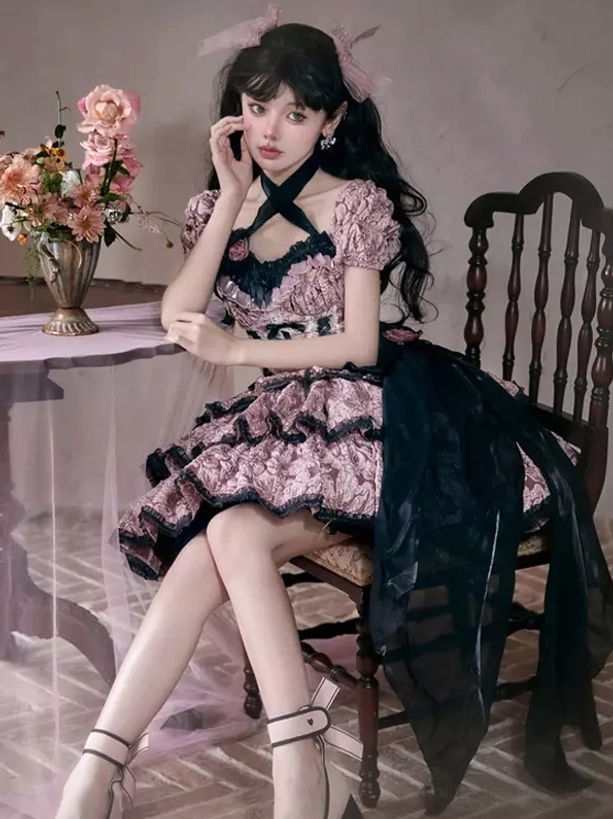 Gothic Lolita floral dress showing cross halter back detail, black side sash accent, ruffled silhouette, vintage indoor setting with furniture and floral decor