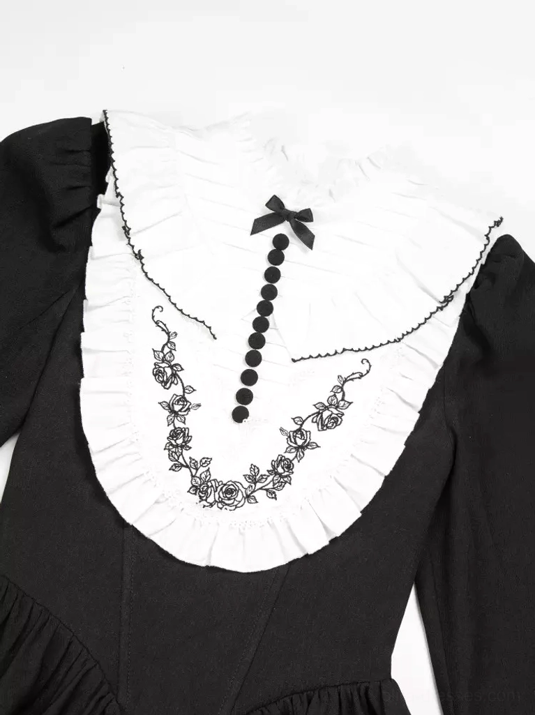 Close-up detail of Gothic Lolita dress collar featuring white ruffled edge, black bow accent, and intricate floral embroidery with button-tassel trim