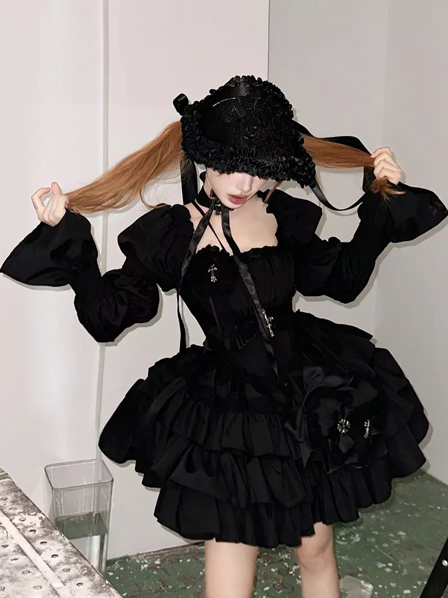 Model posing in black Gothic Lolita dress with ruffle bucket hat, off-shoulder puff sleeves, multi-layered ruffle skirt, cross embellishments, twin ponytails, indoor studio portrait