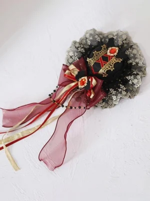 Flat lay top-down view of Gothic Lolita hair fascinator displaying embroidered lace ruffle, multi-layer bow structure, beaded chain details, and faux gemstone ornaments