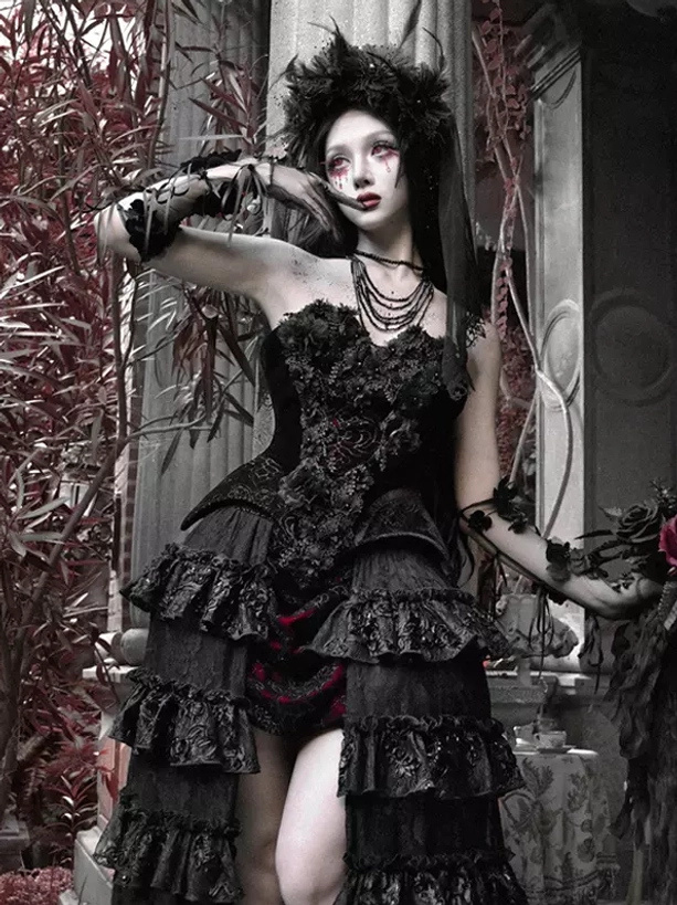 Gothic black and red lolita gown with lace arm cuffs and layered ruffled train skirt, half front angle featuring model with feathered gothic headpiece and red foliage backdrop