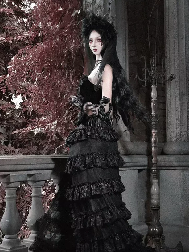 Black and red gothic lolita gown with lace arm cuffs and layered ruffled train, half side angle showing model holding floral decor in red foliage scenic background