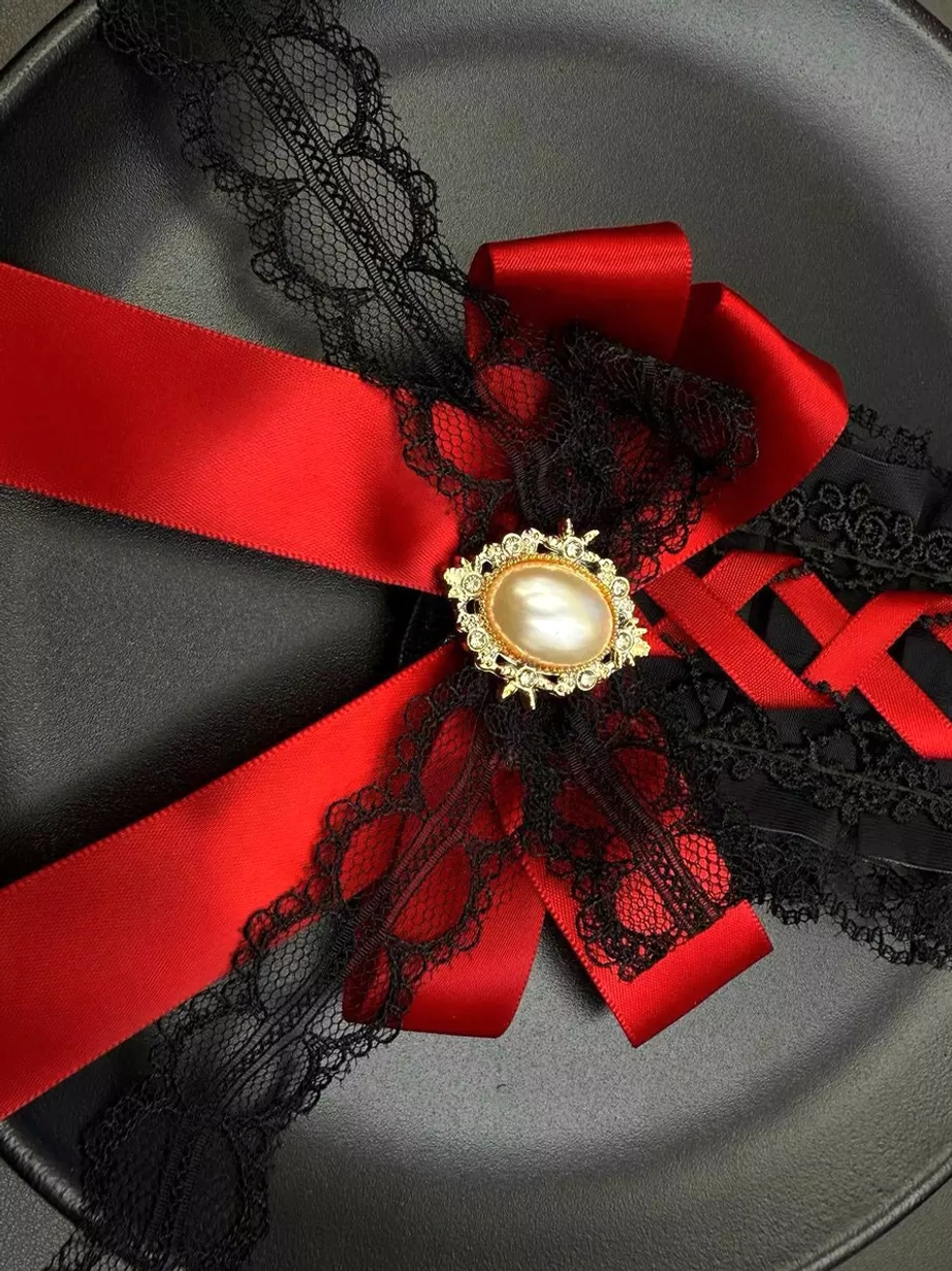 Close-up top-down view of gothic lolita hair accessory revealing the cross-shaped red satin bow construction and intricate black lace trim details on matte surface