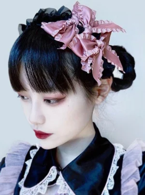 Gothic lolita hair bow headband with black ruffled edges and pink multi-layer satin bows worn by model in maid-style lolita outfit left three-quarter profile view