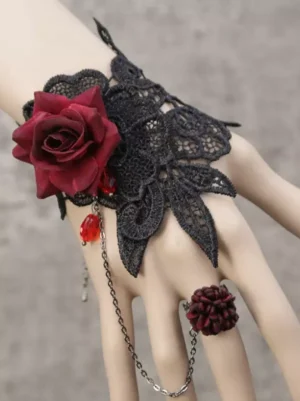Gothic Lolita hand chain bracelet featuring black guipure lace cuff with oversized burgundy velvet rose and crimson teardrop gemstone, three-quarter view on mannequin hand against gray studio background