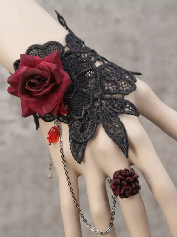 Gothic Lolita hand chain bracelet featuring black guipure lace cuff with oversized burgundy velvet rose and crimson teardrop gemstone, three-quarter view on mannequin hand against gray studio background