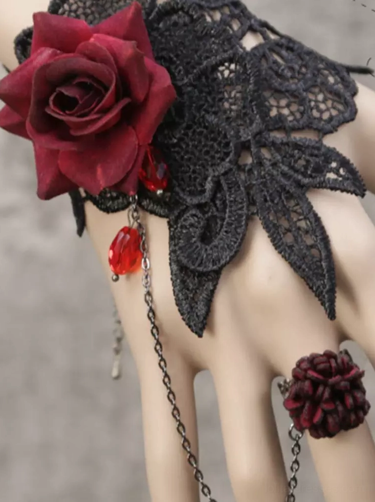 Close-up overhead view of Gothic Lolita hand chain bracelet displaying oversized burgundy velvet rose, intricate black guipure lace applique, crimson teardrop charm pendant, and chain-attached flower ring detail
