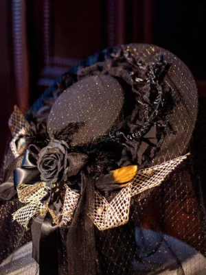 Front close-up detail of gothic lolita headdress featuring sparkly black hat crown, black rose, satin ribbon trim, and feather decorations on elegant lolita headpiece