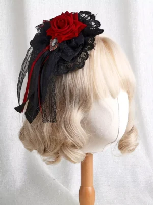 Gothic Lolita headdress with red velvet rose and black lace on blonde curly wig mannequin, front three-quarter view showing gem brooch and red-black ribbon sashes