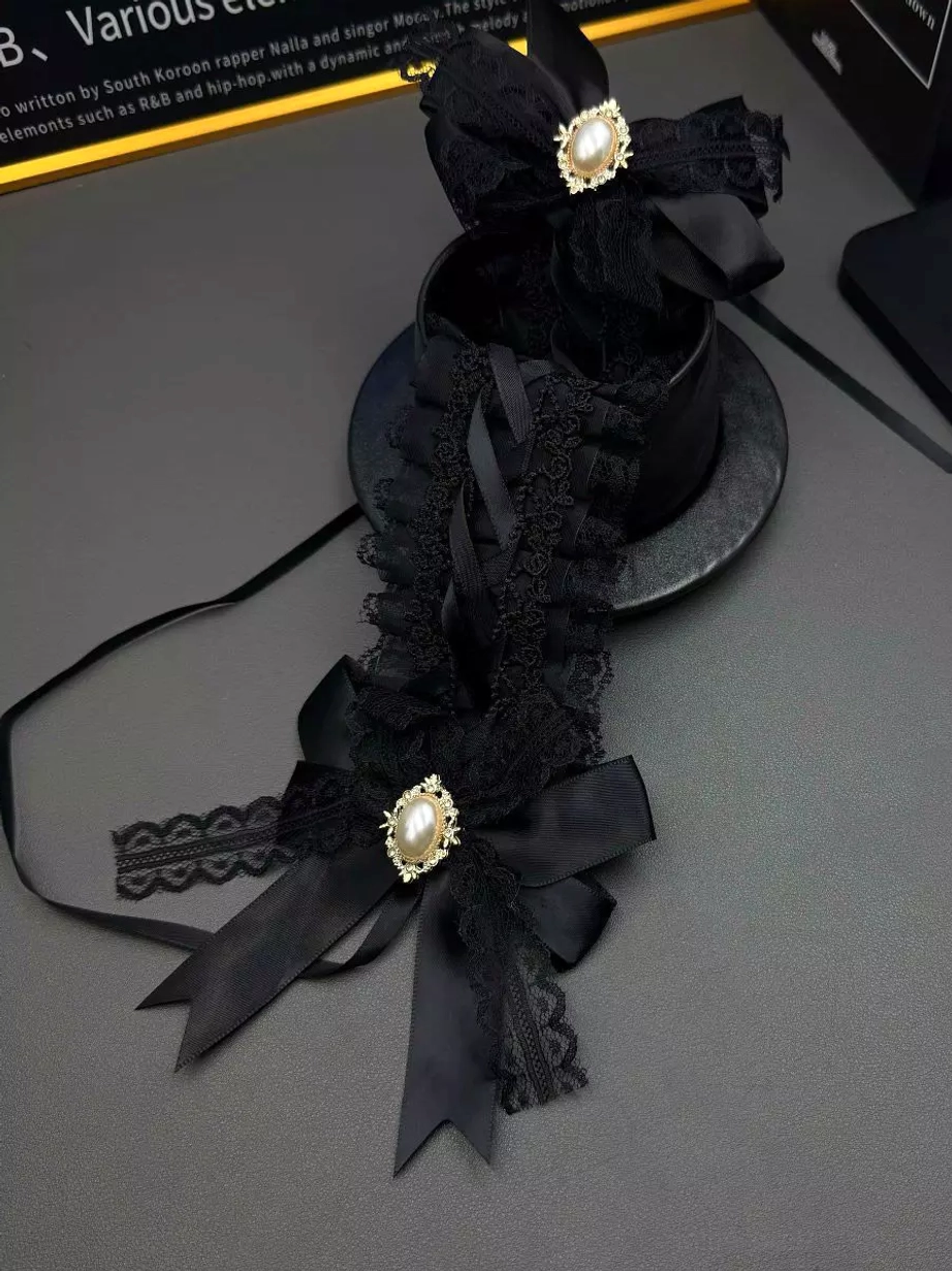 Gothic lolita headpiece styled in dark aesthetic setting with black satin bows, black lace trim, gold-tone pearl brooches, and mini top hat prop for gothic fashion inspiration