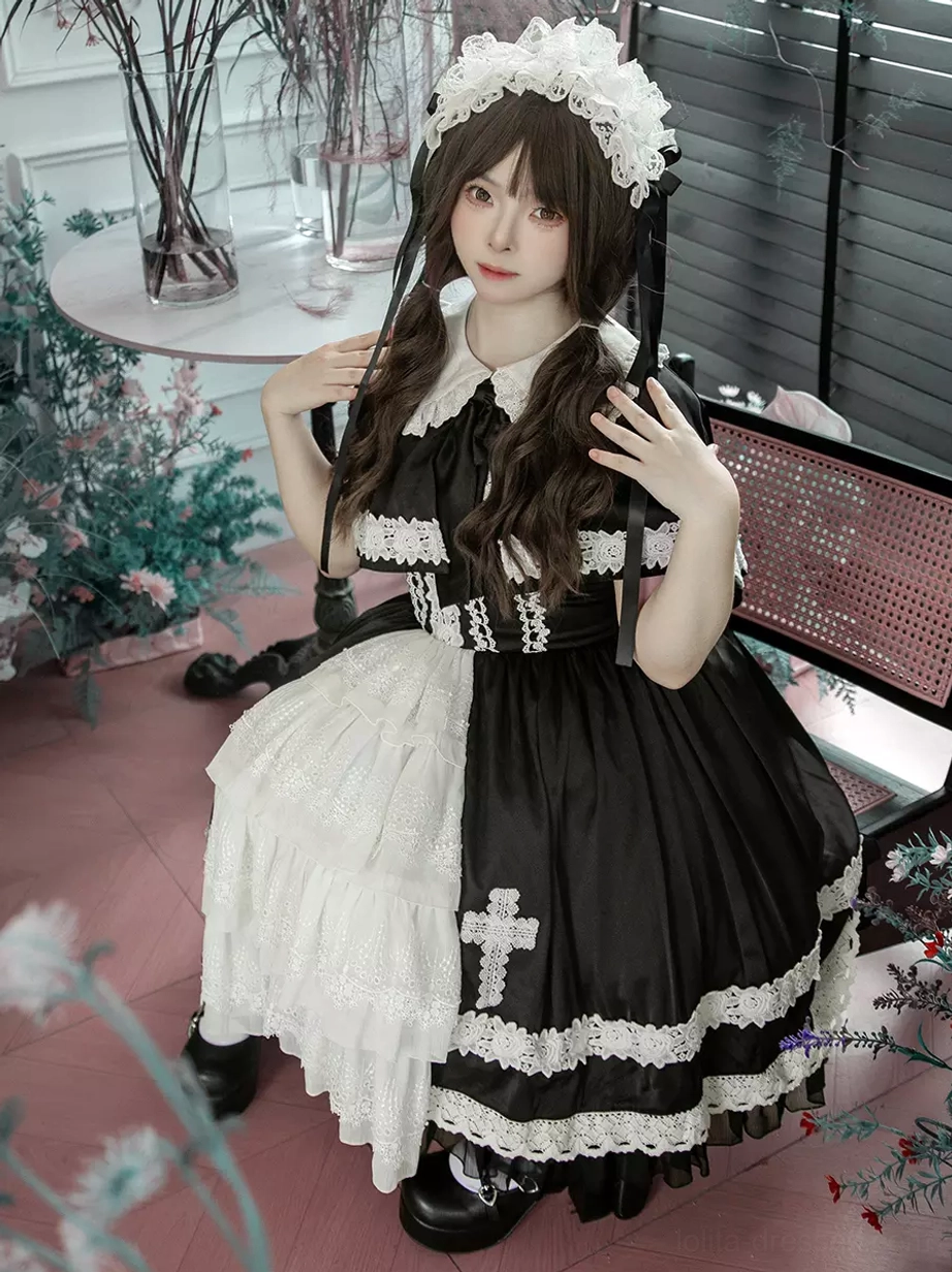 Full side-seated view of gothic lolita JSK dress showing asymmetric dual-tone skirt construction, cross applique on black skirt portion, and soft warm lighting aesthetic