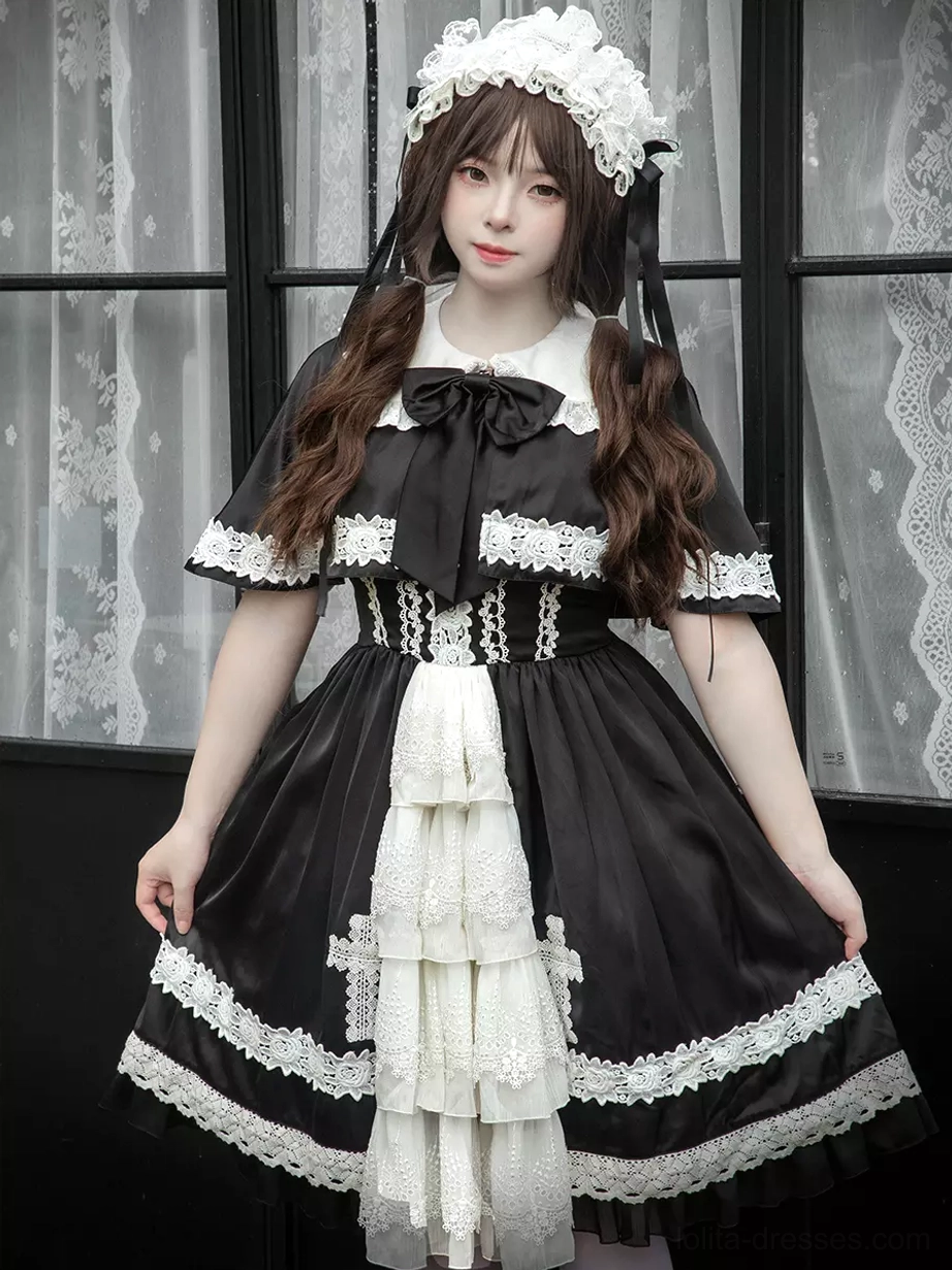 Full front view of classic gothic lolita JSK dress with layered white ruffled front panel, black skirt, cross lace appliques, Peter Pan collar with bow, and lace trim details