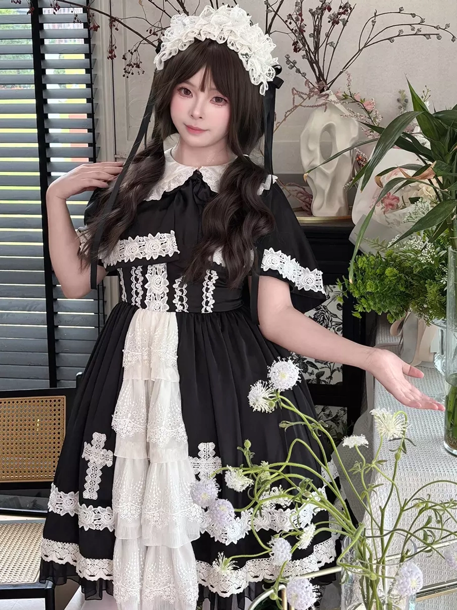 Half-body three-quarter view of gothic lolita dress with cross lace appliques on black fabric, layered white front skirt panel, and comprehensive lace trim on all edges