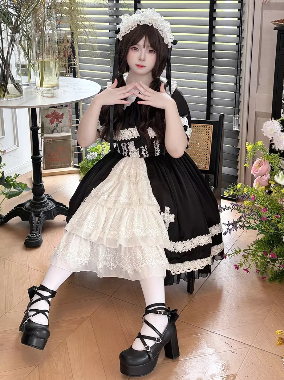 Three-quarter seated front view of gothic lolita dress in retro cafe background, featuring long layered white ruffled skirt section, cross embroidery on black skirt, and platform buckle shoes