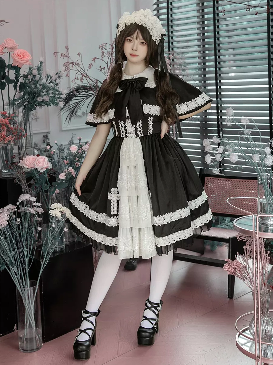 Full front standing view of gothic lolita dress with decorative neck bow, cross embroidery on skirt hem, layered white front panel, and lace embellishments throughout