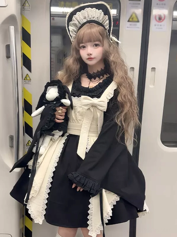 Three-quarter front view of black Gothic Lolita maid dress with large cream bow, irregular hem lace apron, held with plush toy accessory