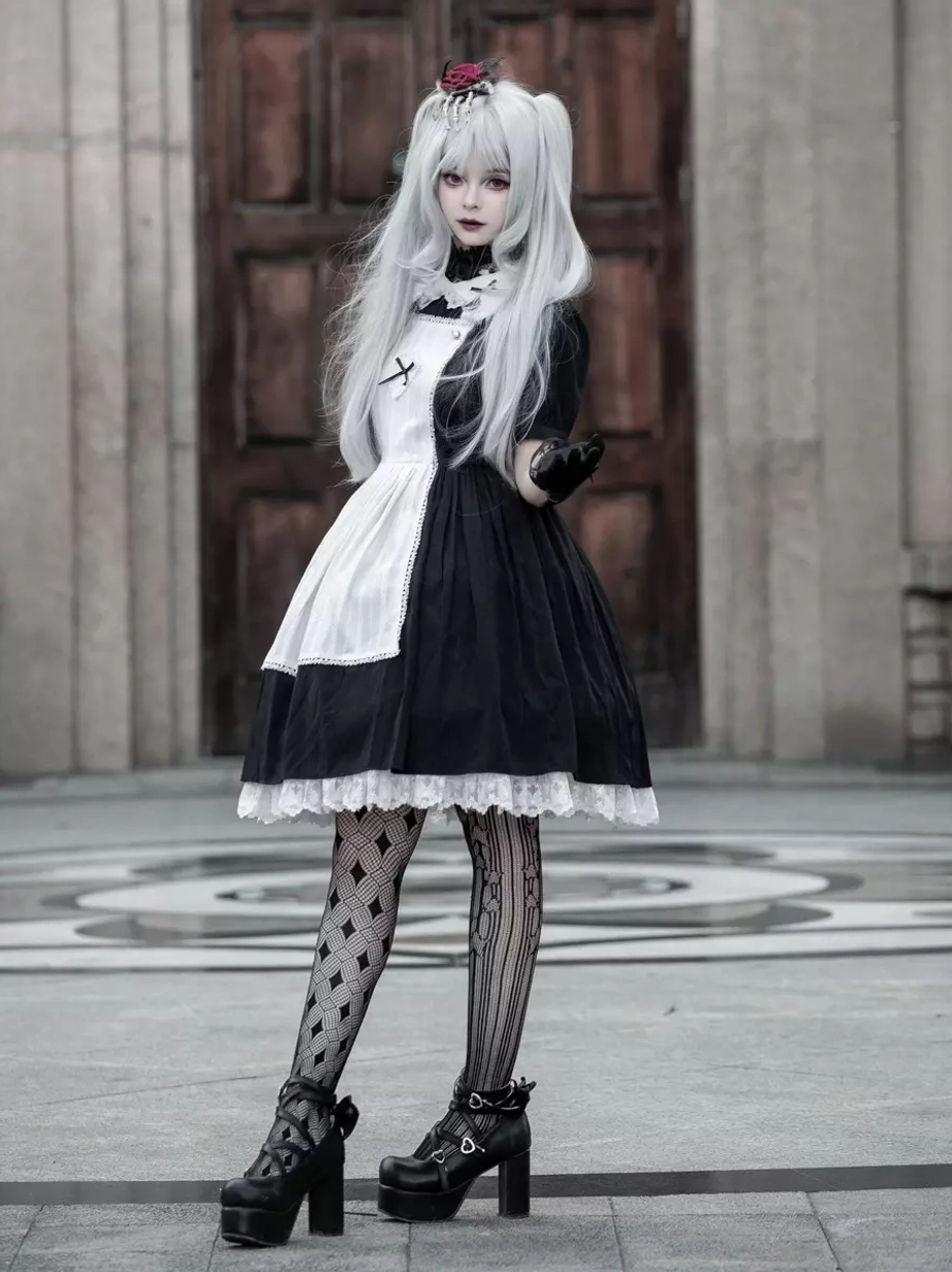 Side profile view of Gothic Lolita maid dress, striped pattern stockings, one hand on waist, full silhouette from waist down, outdoor stone background