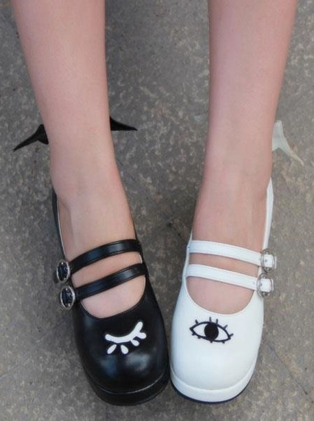 Front top view of worn Lolita Mary Jane shoes showing mismatched black and white colorways dual buckle straps and cute face prints on feet concrete background