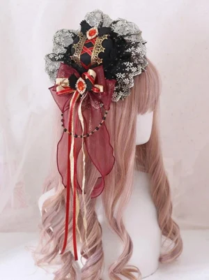 Gothic Lolita mini top hat fascinator hair clip worn side view, showing black lace bow with wine red and gold embellishments, beaded chains, and ribbon tassels on pink curled hair
