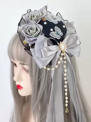 Gothic lolita mini top hat headdress with grey rose embroidery and pearl tassel bow worn on mannequin with ash grey long hair, left profile view showing black fabric base and butterfly embroidery details