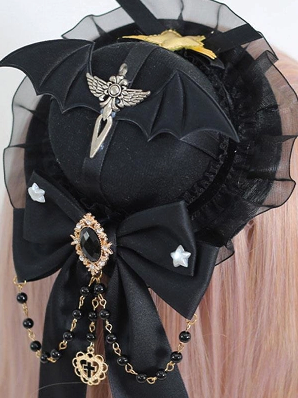 Gothic lolita mini top hat hairclip close-up front view on pale pink mannequin hair showing bat wing brooch large gem bow and bead chain tassel details