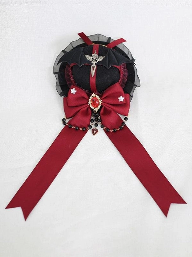 Gothic lolita mini top hat hairclip flat lay top view showing black base with wine red bow star embellishments and gem brooch centerpiece