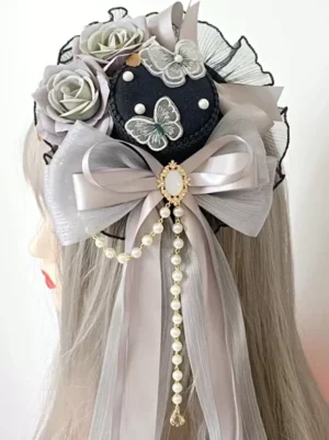 Rear left profile view of gothic lolita mini top hat headdress displaying back design with pearl studs on black base, matching decorative bow tassel attachment, styled on mannequin with ash grey hair