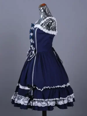 Left side view of navy gothic lolita jumpskirt displaying white lace shoulder straps, small side bows, and tiered ruffled skirt with delicate lace hem detail