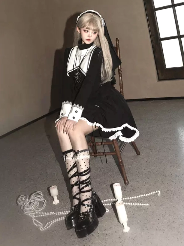 Side profile seated view of black and white gothic lolita dress displaying bow-decorated white cuffs, asymmetric high-low hem with white frill trim, and cross pendant, indoor candle ambiance