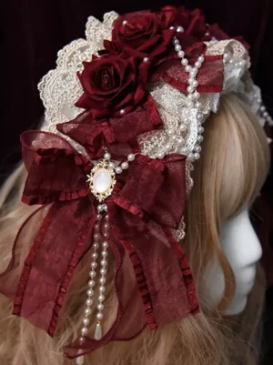 Gothic Lolita headband side three-quarter view showcasing large burgundy organza bow with gem brooch centerpiece and dangling pearl tassels