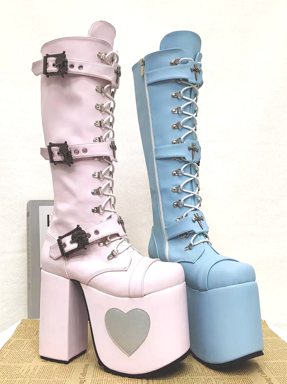 Front-side oblique view of Gothic Lolita platform knee-high boots with extra thick platform heel, side zipper closure, and cross-style metal buckles on kraft paper box background