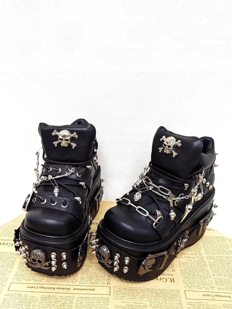 Front three-quarter view of gothic platform lolita boots decorated with metal skull studs chain laces and spike straps showing dramatic wedge platform silhouette