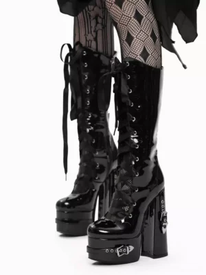 Three-quarter front angle of gothic lolita boots showcasing shiny patent leather material, branded metal heel details, front ribbon lacing system, paired with diamond-pattern fishnet tights and black draped skirt