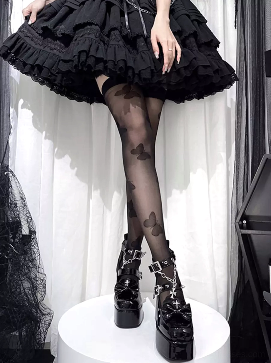 Model wearing gothic lolita platform boots with ruffled black skirt and patterned butterfly stockings lower full leg view
