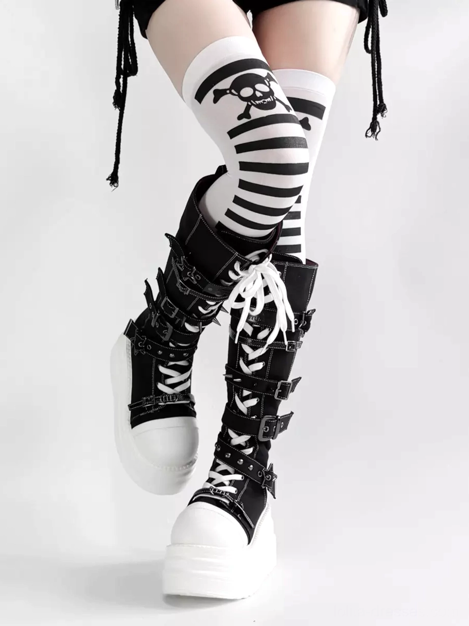 Low front angle of black lolita platform boots with white platform toe cap and lace-up closure worn with black and white skull stripe over-the-knee socks