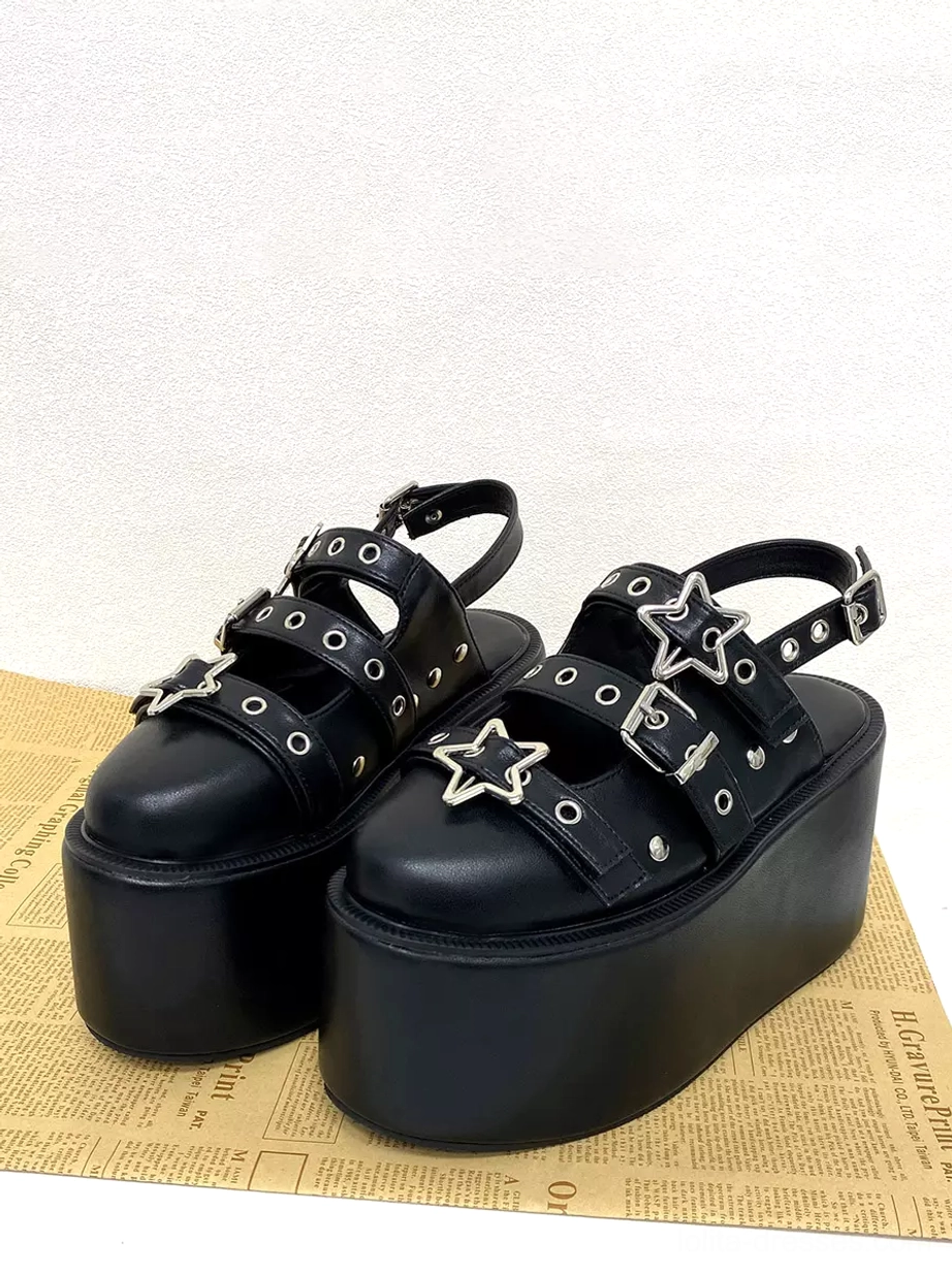 Paired black gothic lolita platform sandals with double buckle straps and star decorations on newspaper print background