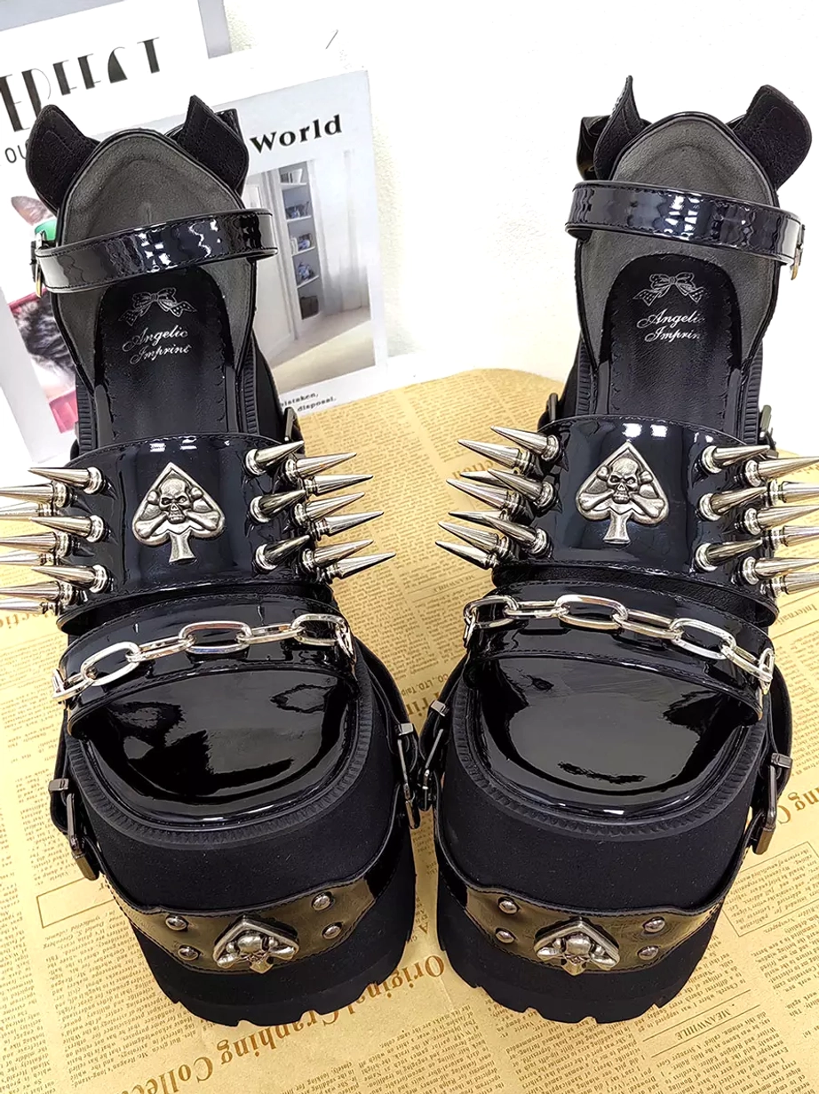 Pair of gothic lolita platform sandals front flat view displaying spade skull emblems, long spike studs across upper, silver chain straps, and patent leather toe caps on black leather