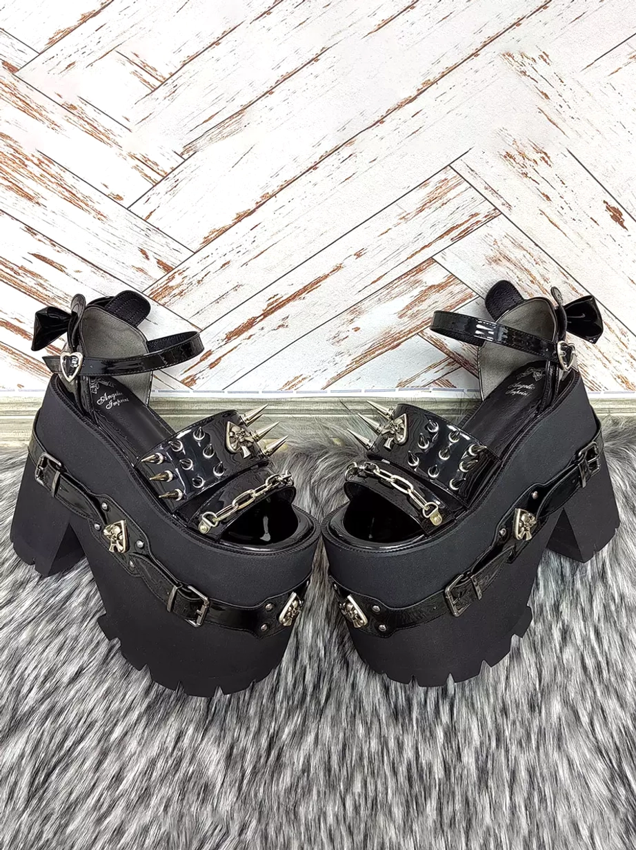 Pair of gothic lolita chunky heel sandals low top side view showing mixed matte and patent black leather finish, spike decorations, spade skull buckles, and architectural wedge platform construction