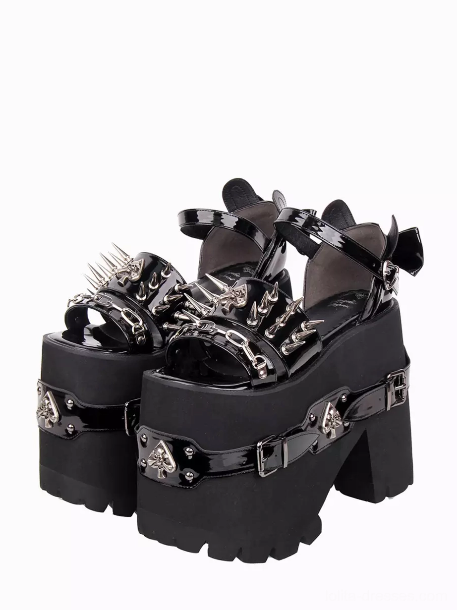 Gothic lolita chunky platform sandals with spike studs and spade skull metal buckles, front three-quarter view, black PU leather open toe design with decorative ankle strap and bow detail